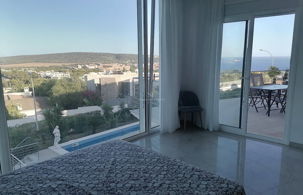Chambre principale avec sol en marbre poli et baies vitrées ouvrant sur une terrasse dominant la mer et la piscine.