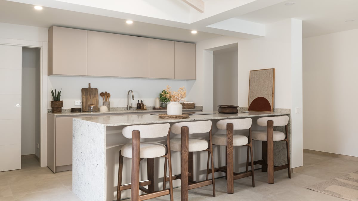 A contemporary kitchen featuring beige cabinetry, a white stone island, and four wood and fabric bar stools.