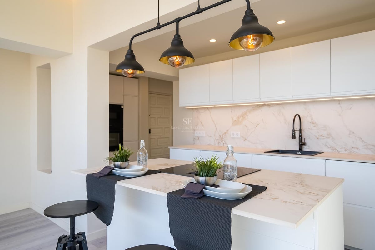 Moderne weiße Küche mit Marmor-Arbeitsplatte und drei schwarzen Industrie-Pendelleuchten.
