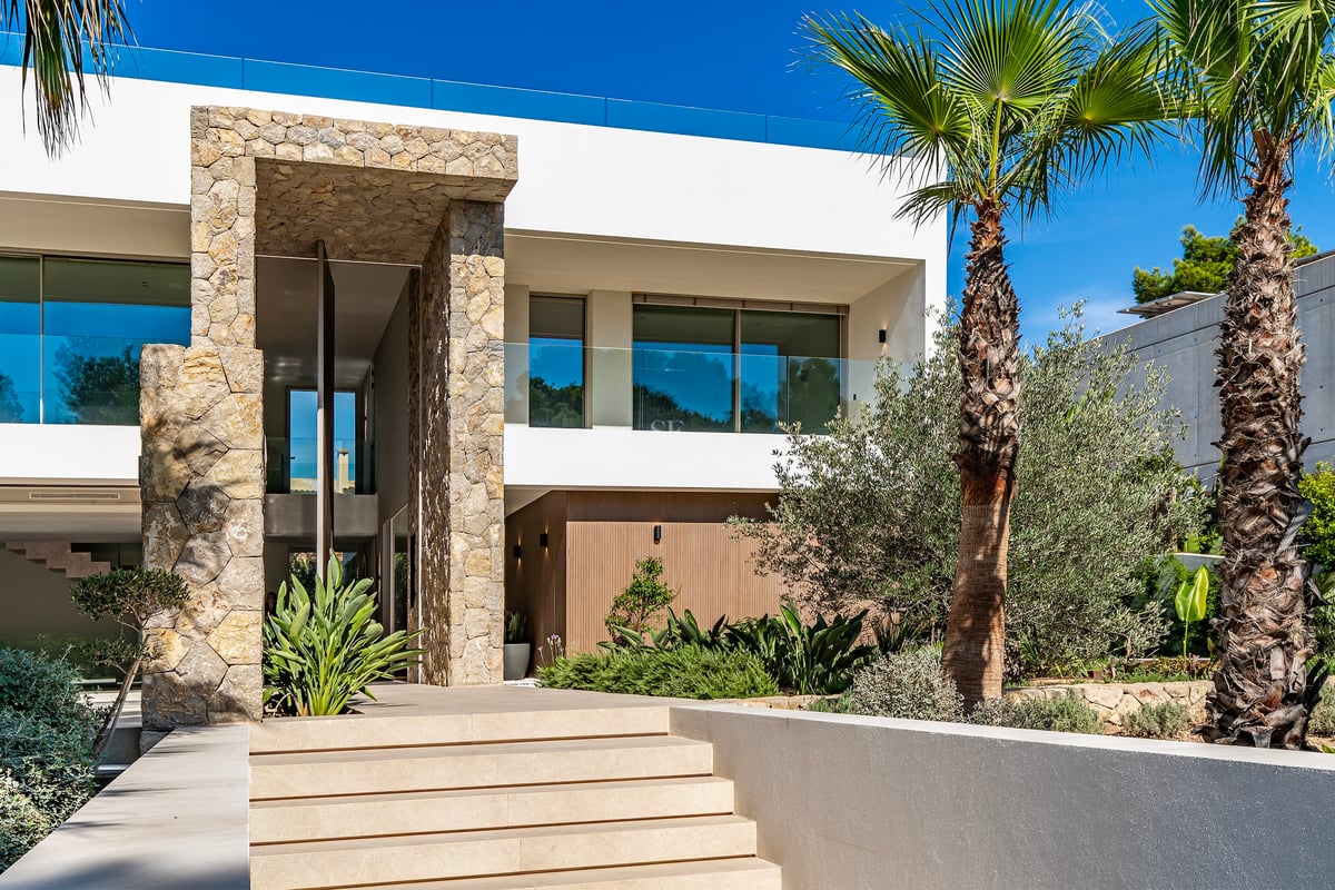 Entrée de villa moderne avec de larges marches en pierre, un haut portail en pierre et des palmiers.