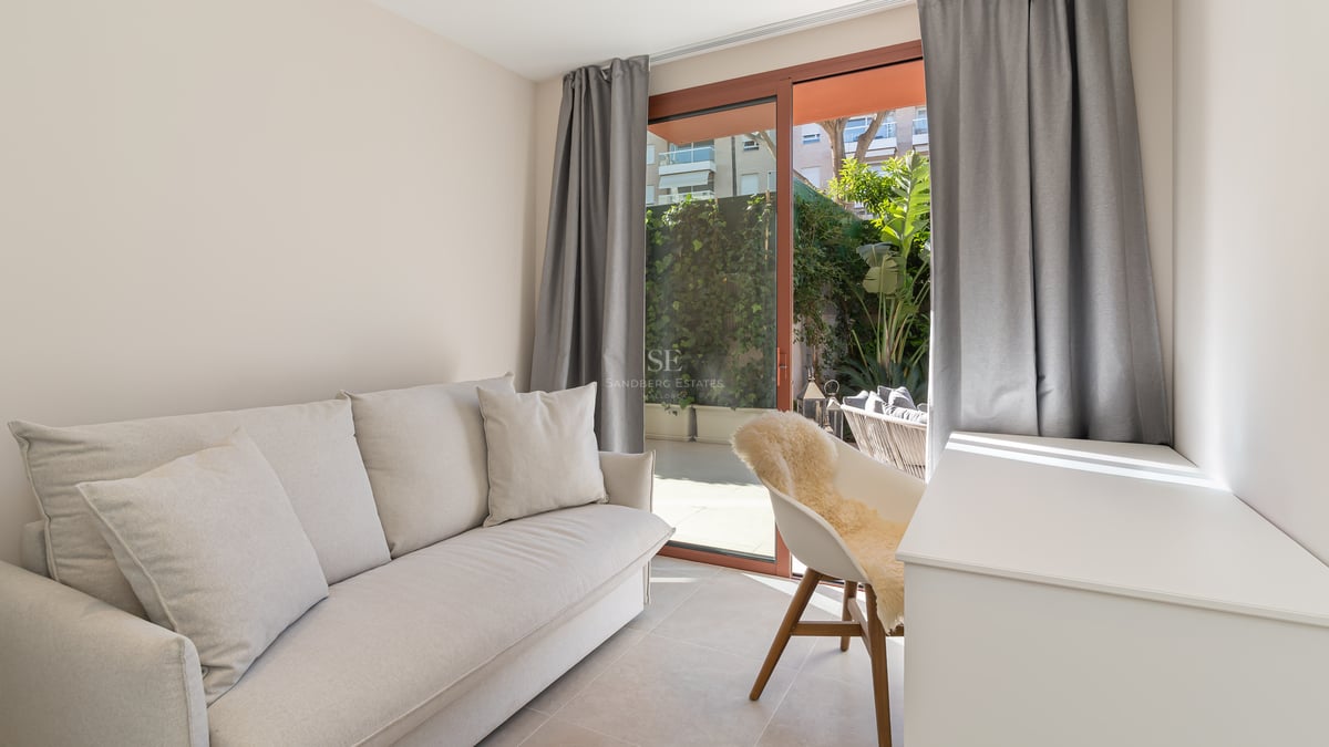 Bright modern room featuring a cream sofa, white desk, and large sliding doors leading to a green private patio.