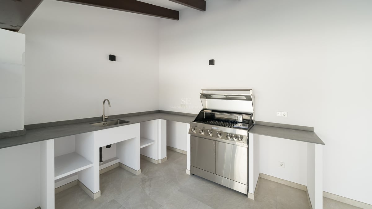 Contemporary outdoor kitchen featuring a stainless steel grill, integrated sink, and sleek gray countertops.