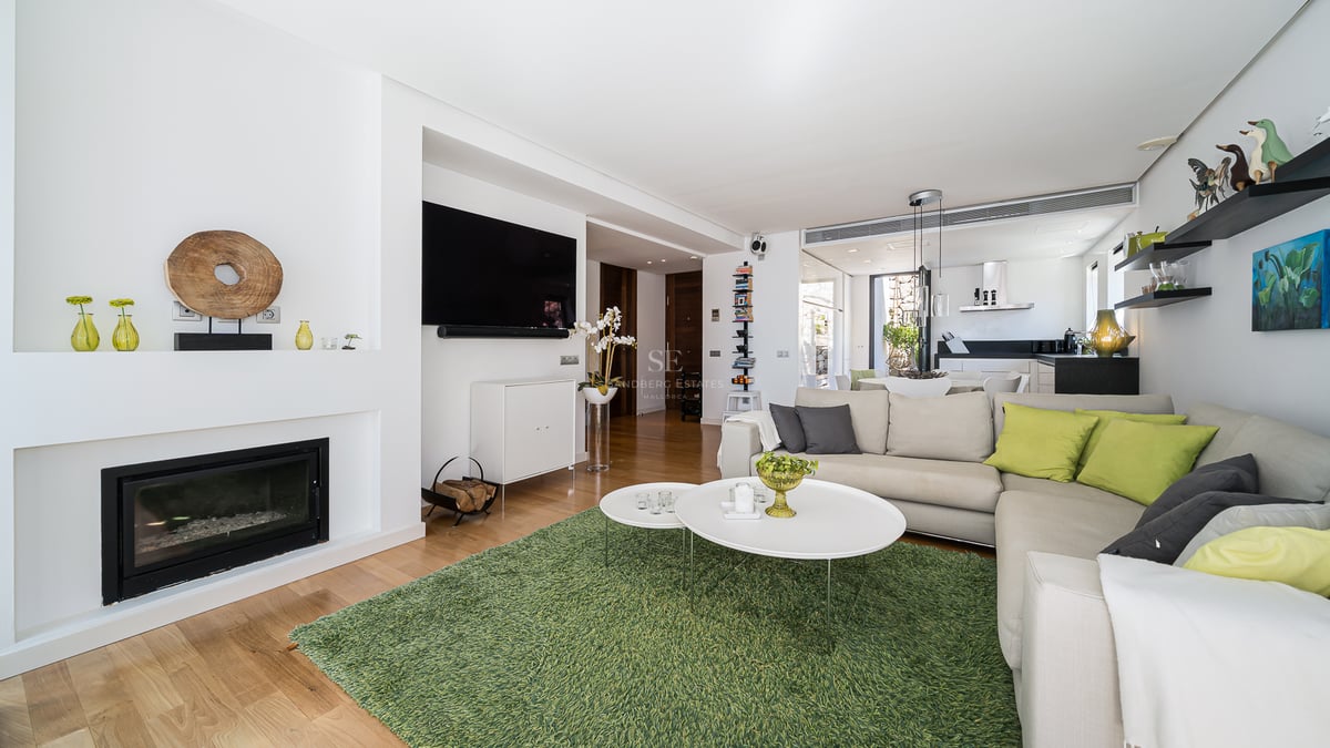 Bright living room with wood floors, L-shaped sofa, modern built-in fireplace, and green rug in an open layout.