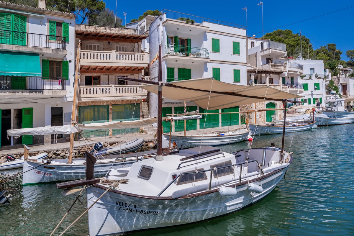 Maisons blanches aux volets verts surplombant un port paisible avec bateaux en bois et eau turquoise.