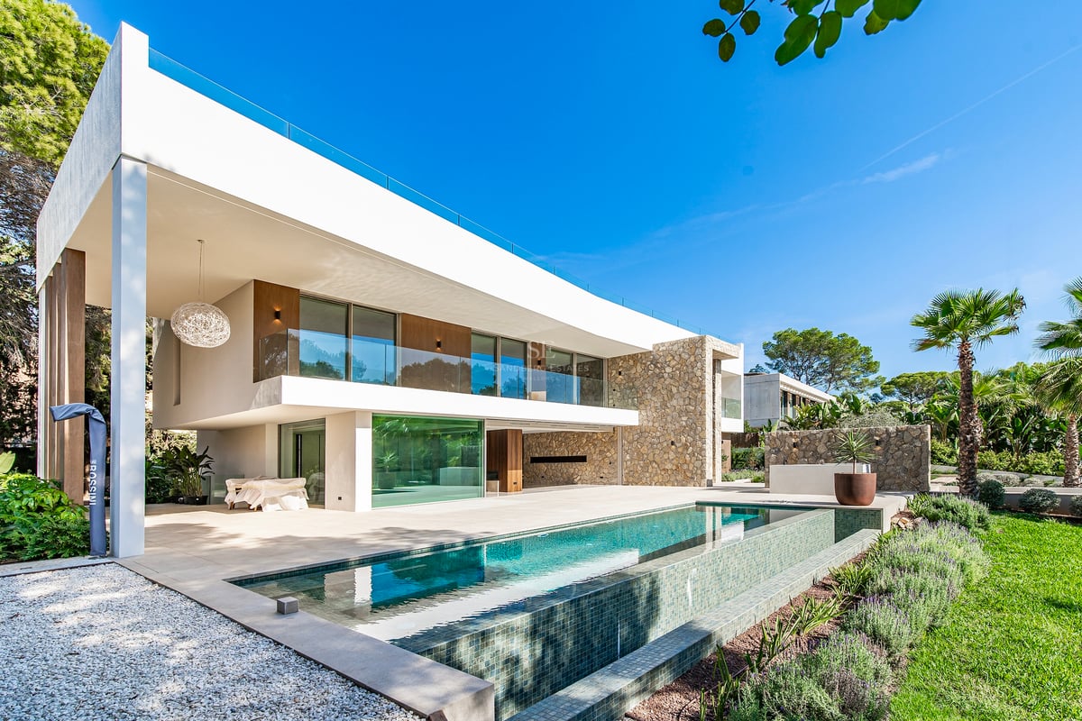 Façade de villa moderne avec piscine à débordement, murs en pierre naturelle et grandes baies vitrées.