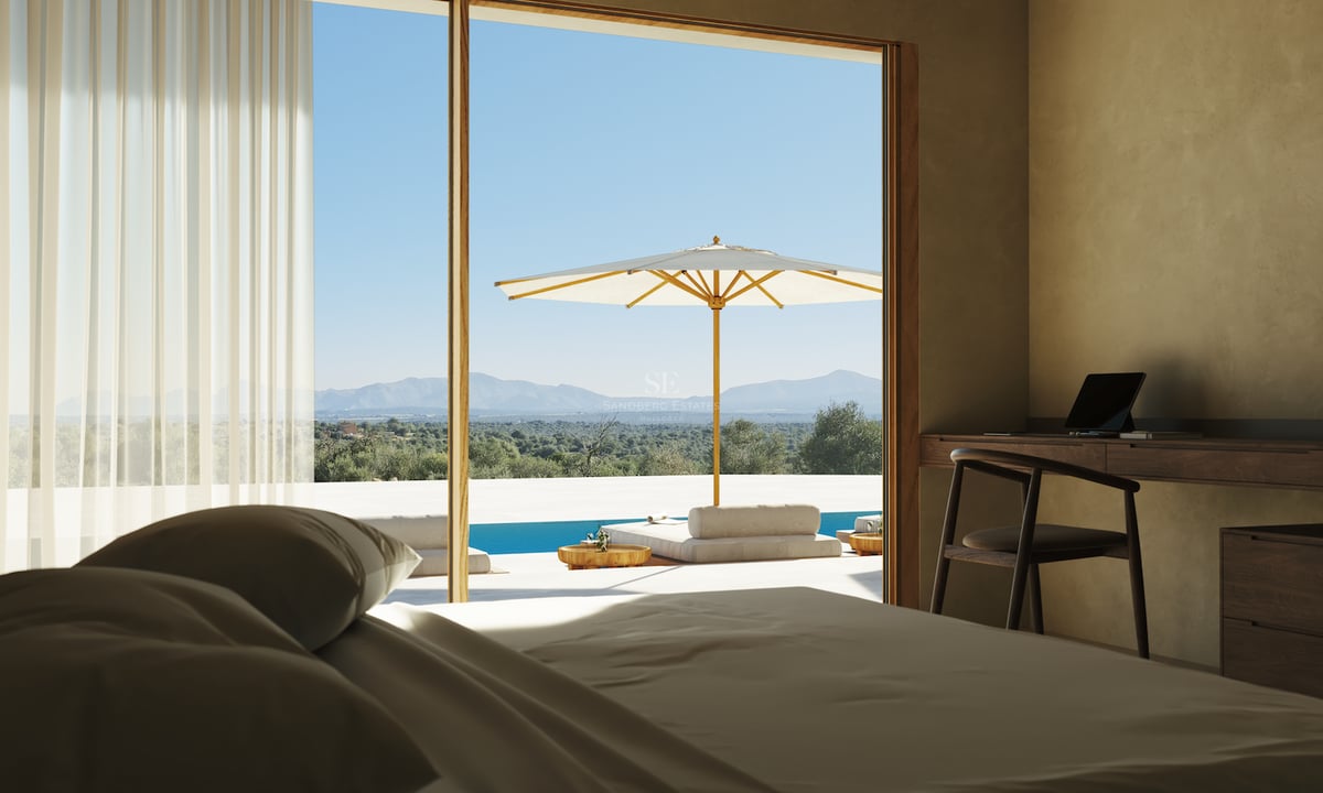 Chambre avec bureau en bois et grandes baies vitrées ouvrant sur une terrasse avec piscine et vue sur les montagnes.