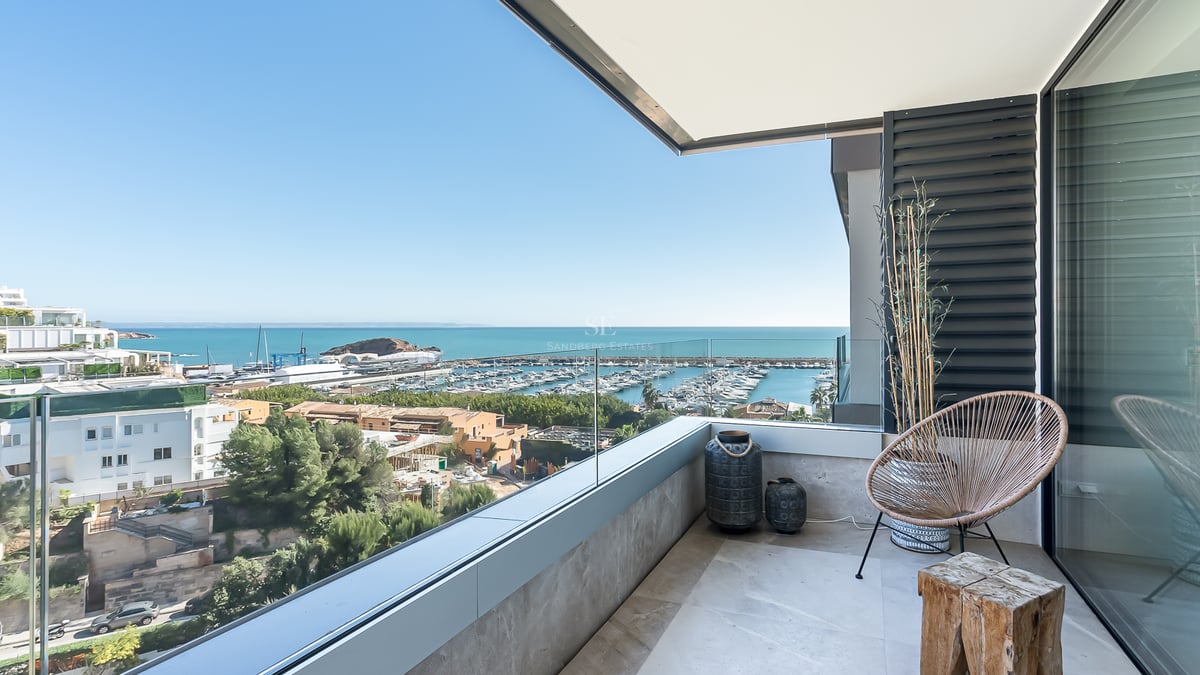 Moderner Balkon mit Glasgeländer und Blick auf einen Yachthafen und das Mittelmeer unter blauem Himmel.