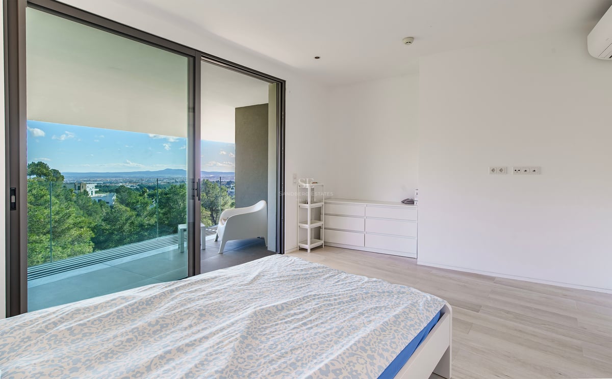 Chambre minimaliste avec grandes portes vitrées ouvrant sur une terrasse avec vue sur la forêt.