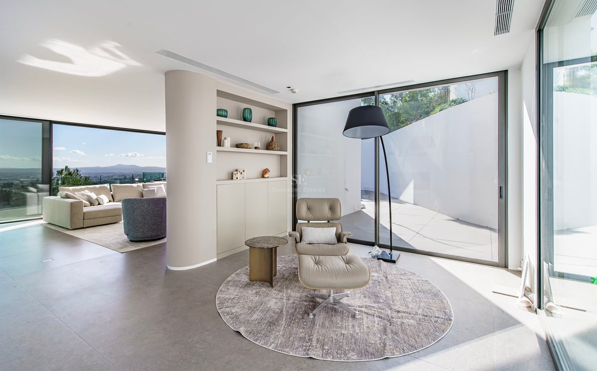 Coin lecture minimaliste avec fauteuil en cuir et baies vitrées offrant une vue sur la ville.