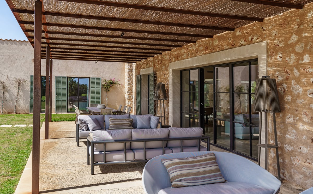 Überdachter Außenbereich mit modernen Sofas, Natursteinwand und Decke mit Holzbalken.