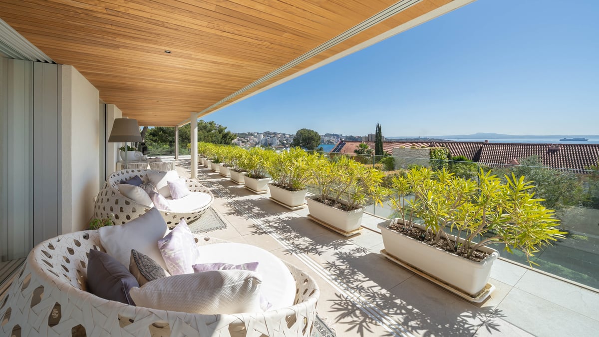 Moderne überdachte Terrasse mit Holzdecke, weißen Loungemöbeln und Pflanzkübeln mit Blick auf das Meer.