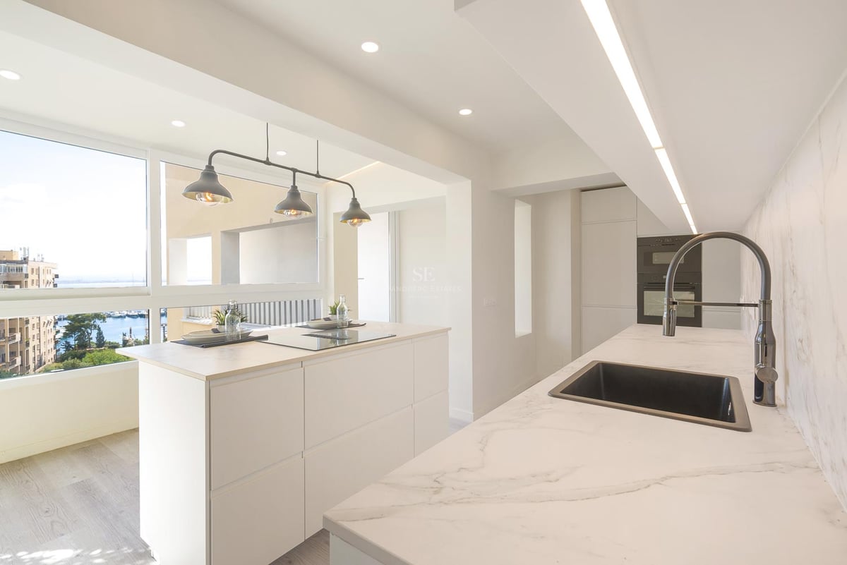 Helle moderne Küche mit weißer Kochinsel, Marmor-Arbeitsplatten und Fenster mit Blick auf einen Yachthafen.