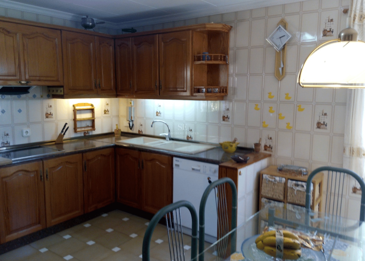 Cocina de estilo rústico con muebles de roble, azulejos decorativos beige y zona de comedor.