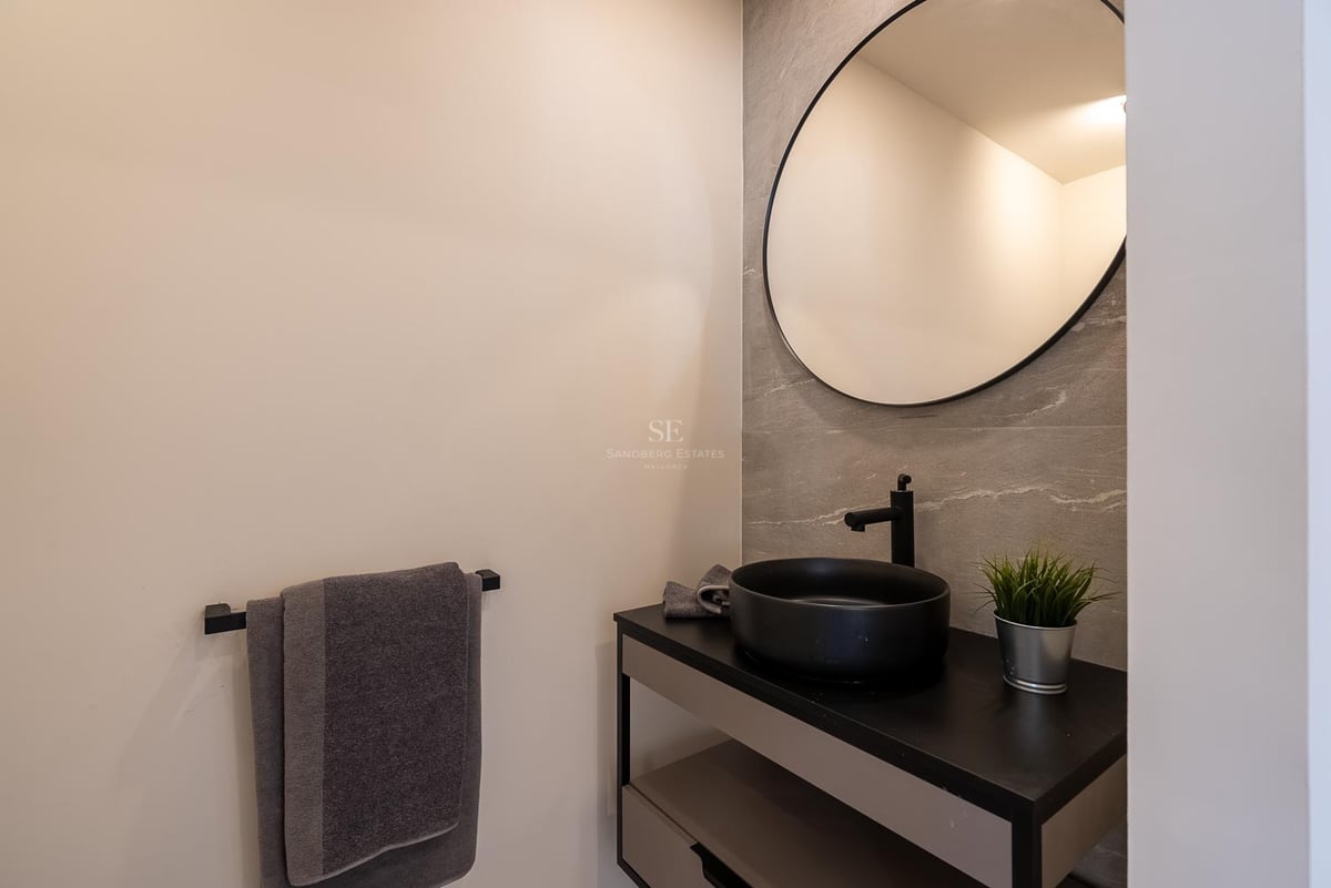 Modernes Badezimmer mit rundem Spiegel, schwarzem Aufsatzwaschbecken und grauen Fliesen in Steinoptik.