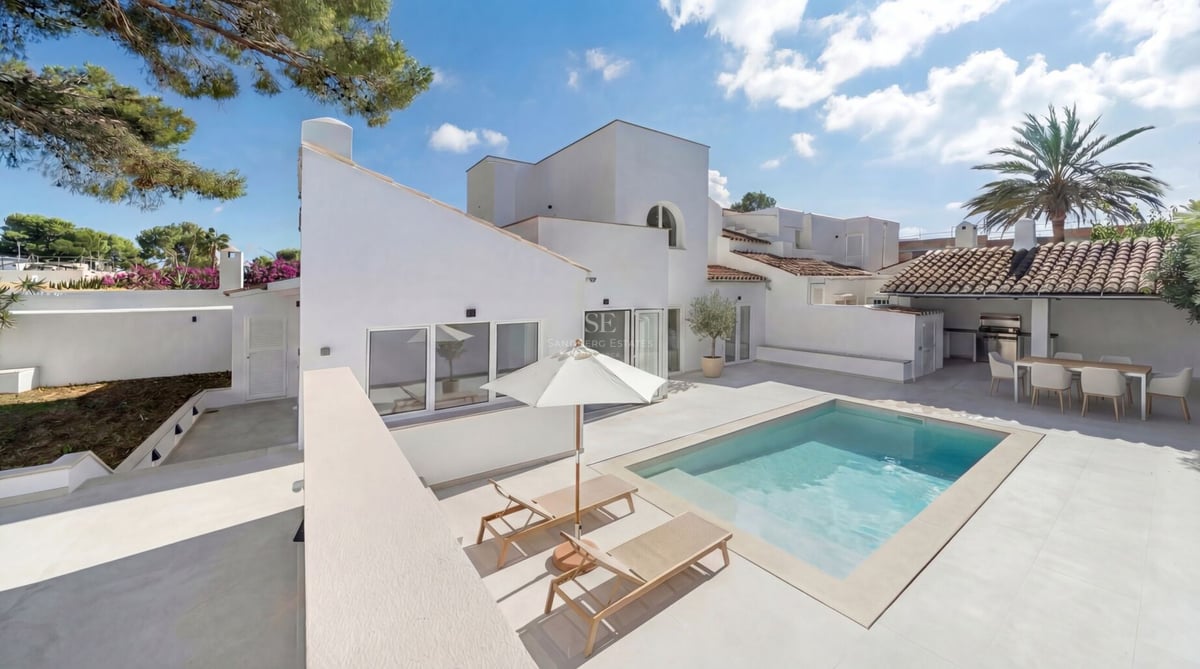 Modern white villa with a rectangular swimming pool, sun loungers, and an outdoor dining area under a tiled roof.