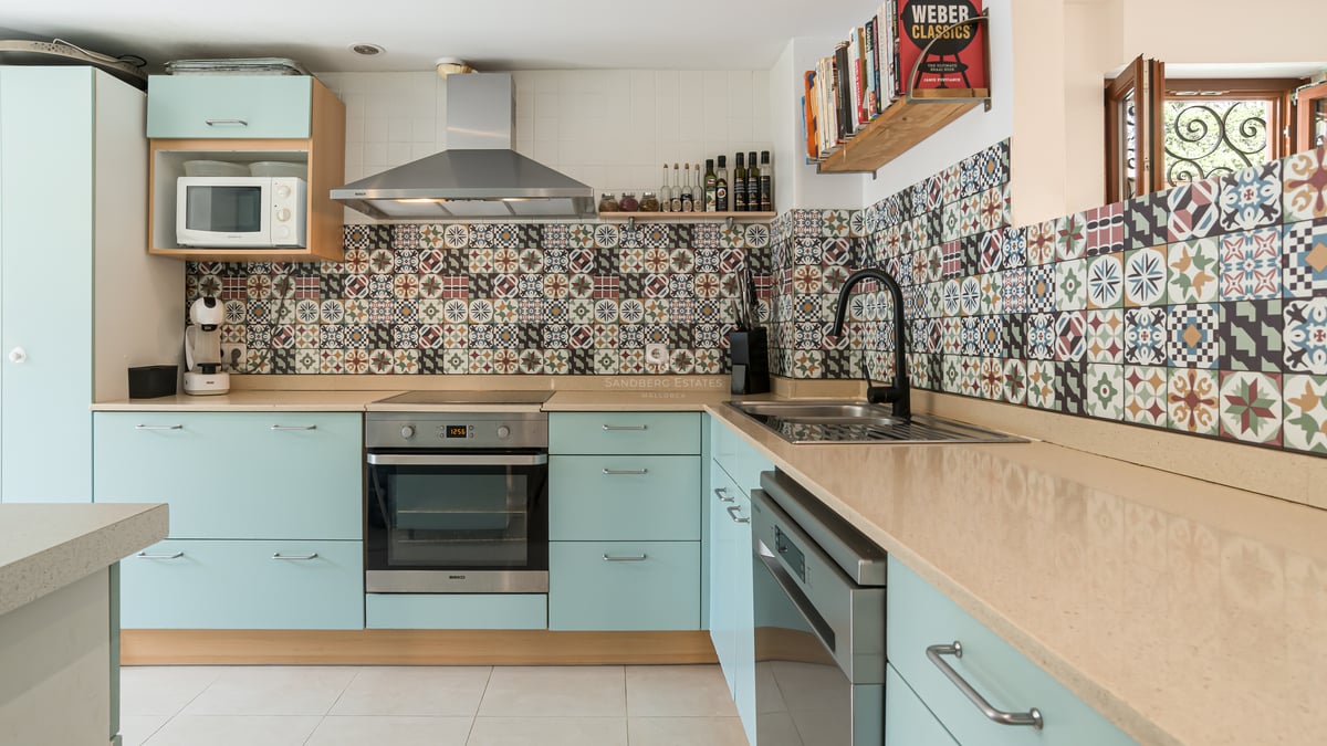 Cuisine avec placards vert menthe, plan de travail beige et crédence en carreaux de ciment colorés.