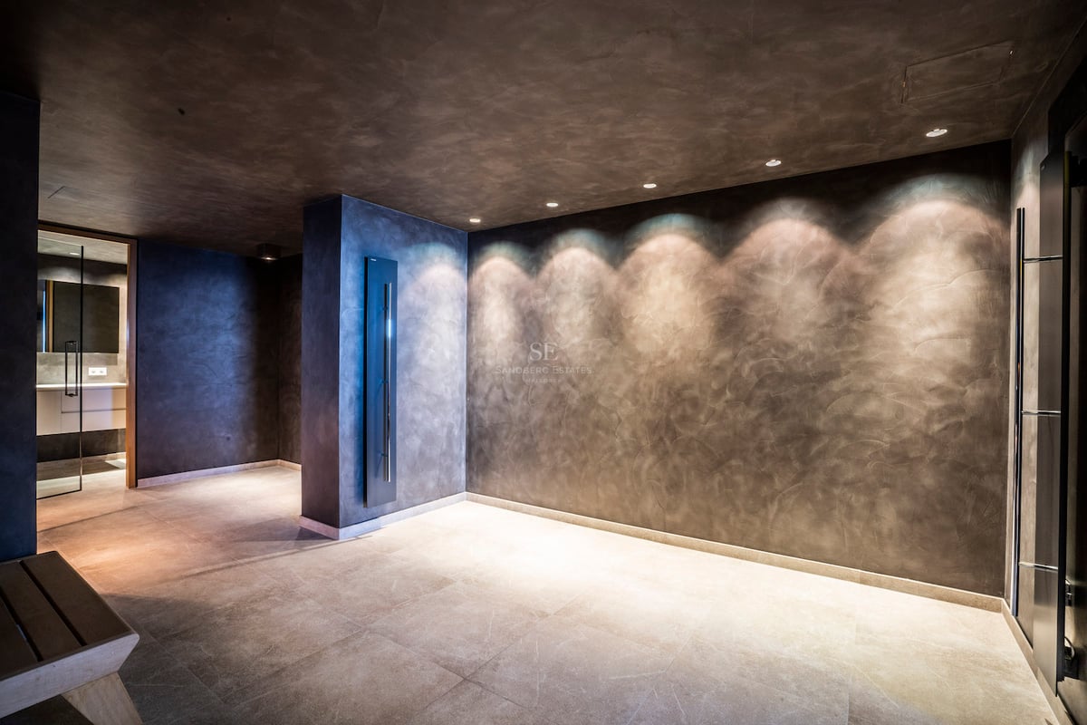 Minimalistischer Spa-Bereich mit dunkel strukturierten Wänden, Spotbeleuchtung und hellem Steinboden.