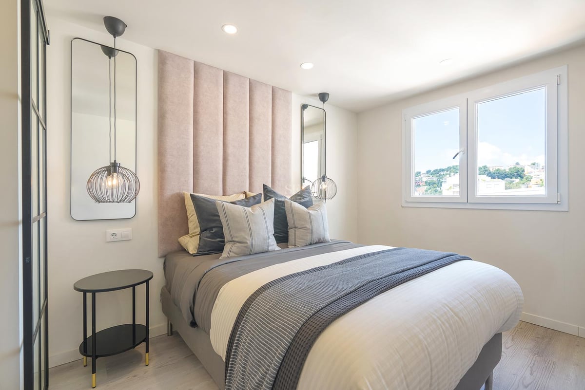 Modernes Schlafzimmer mit altrosafarbenem Kopfteil, Design-Pendelleuchten, grauer Bettwäsche und Fenster.