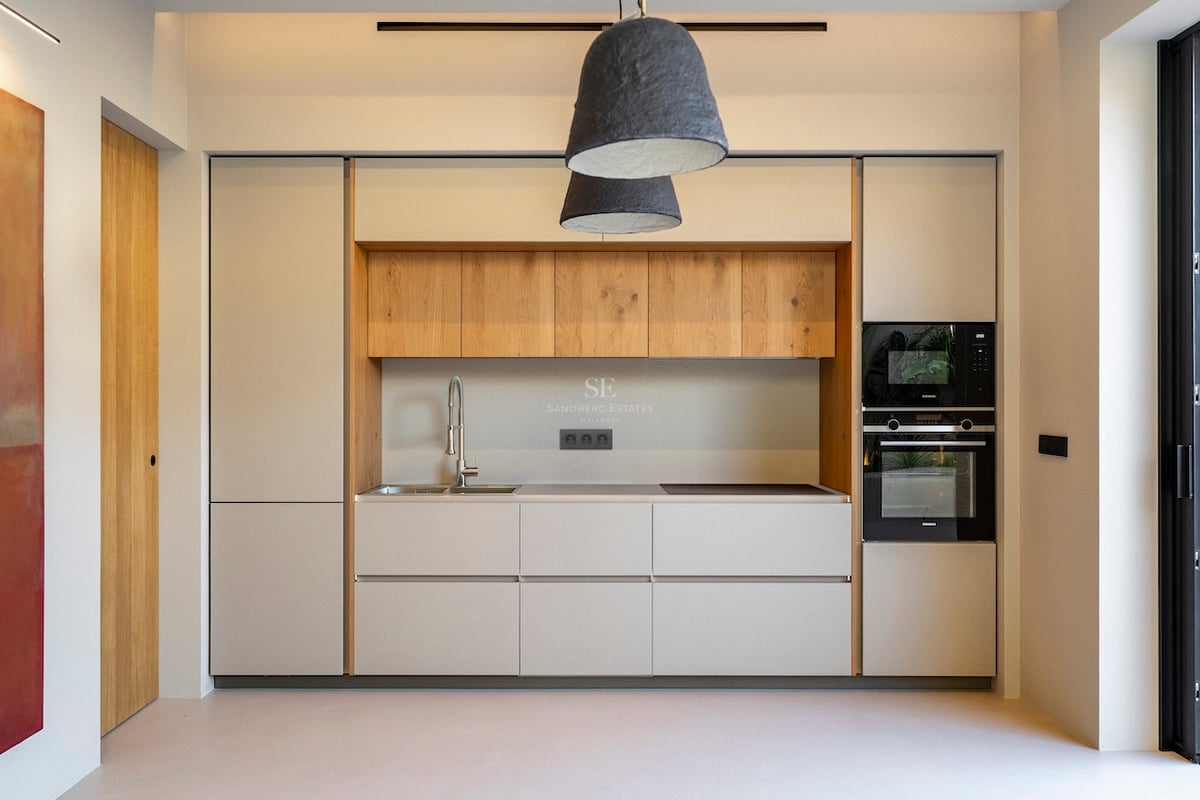 Cuisine moderne aux meubles crème, détails en chêne, appareils intégrés et grandes suspensions texturées.