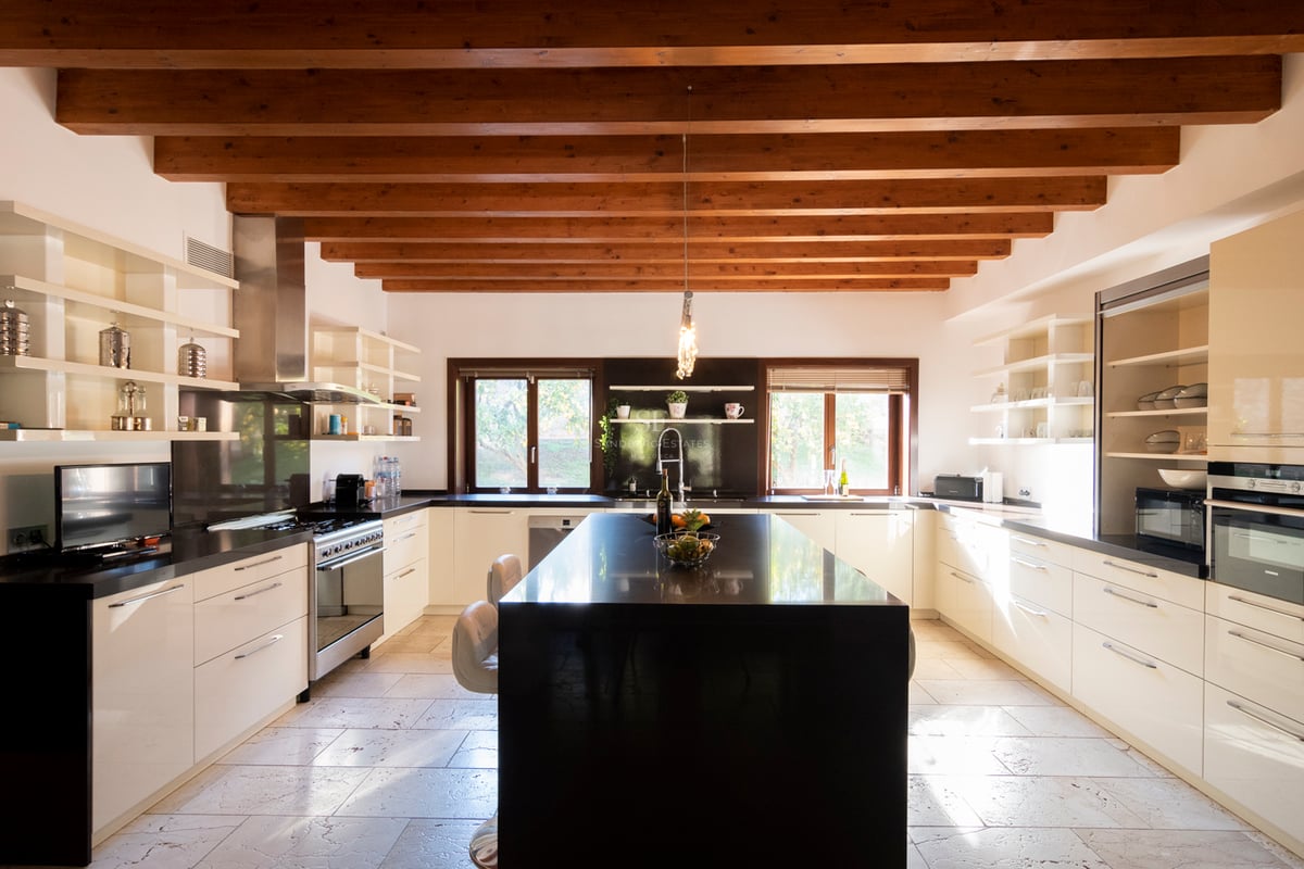 Stort modernt kök med vita skåp, svart granitö och tak med rustika träbjälkar.