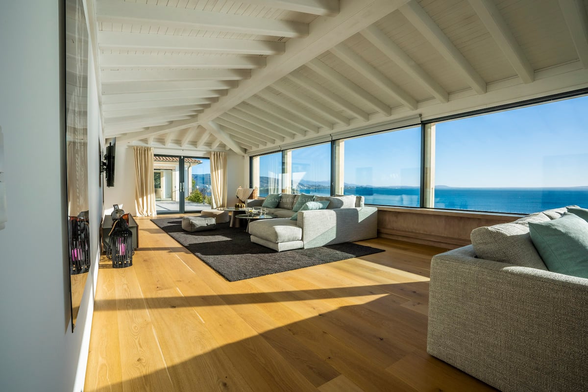 Helles Wohnzimmer mit großen Panoramafenstern mit Blick auf das Meer, weißen Balkendecken und Eichenparkett.
