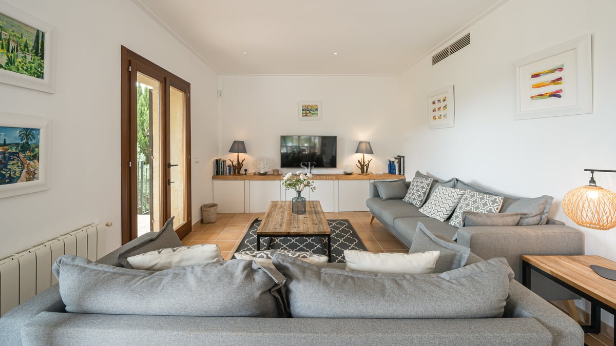 Salon lumineux avec canapé d'angle gris, table basse en bois et portes-fenêtres ouvrant sur le jardin.
