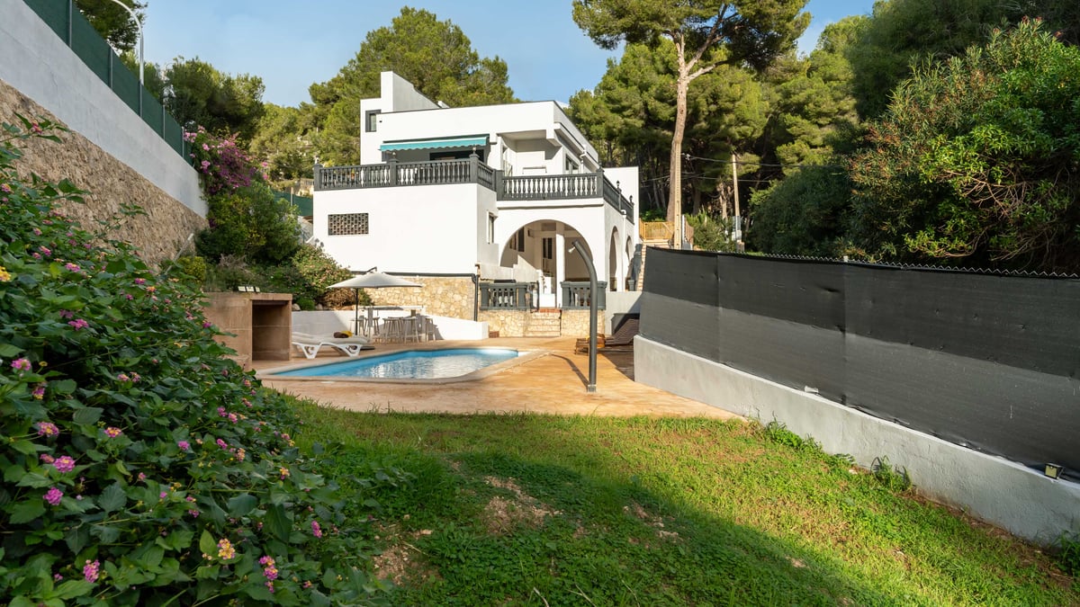 Villa blanche avec piscine privée, terrasse, pelouse et entourée d'une forêt de pins dense.