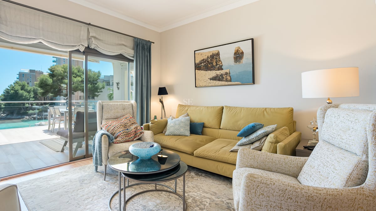 Ljust vardagsrum med senapsgul soffa, mönstrade fåtöljer och skjutdörrar till en solig terrass.