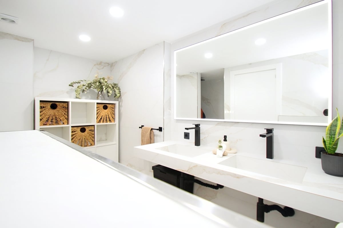 Ljust modernt badrum med dubbelkommod i marmor, mattsvarta kranar och en stor bakgrundsbelyst spegel.