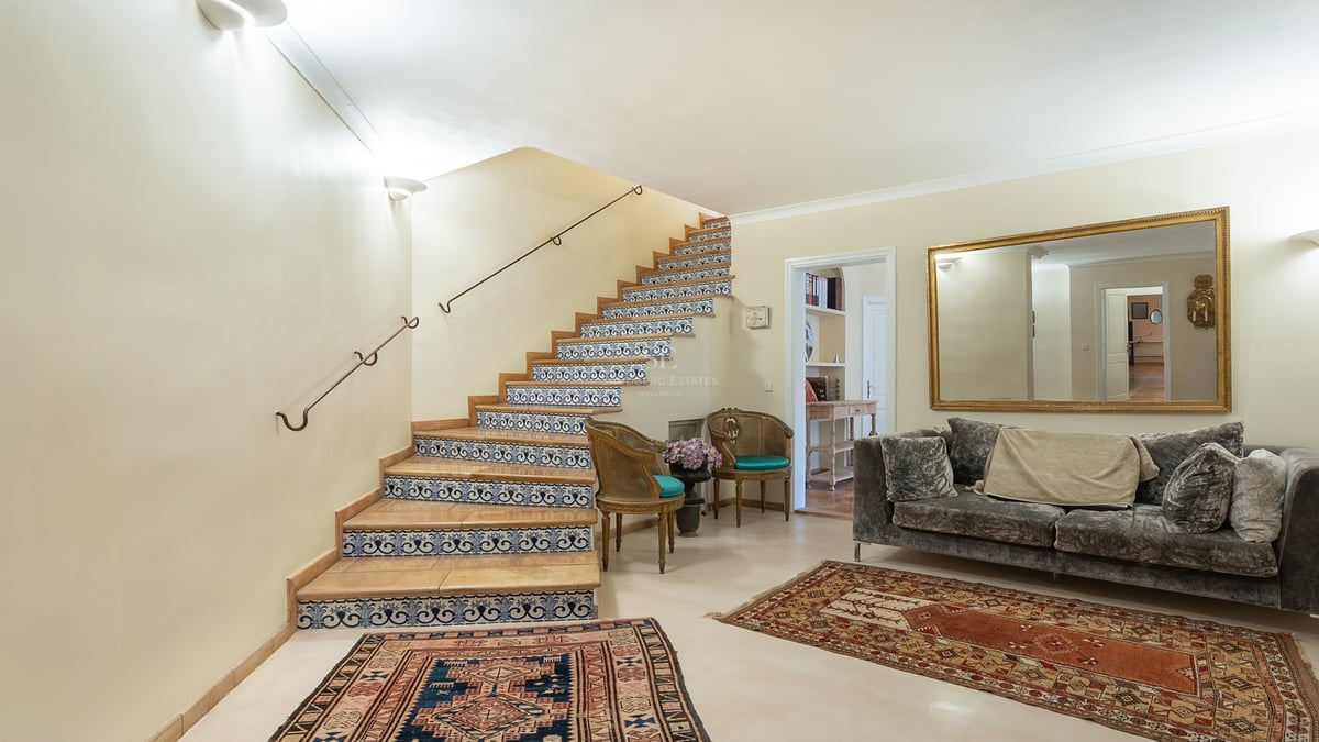 Vue intérieure d'un hall d'entrée avec escalier orné de carreaux bleus et blancs, canapé en velours et tapis.