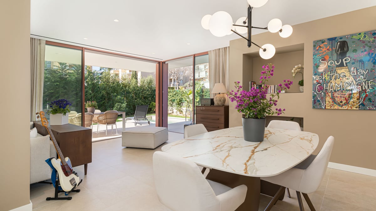 Modern dining area featuring a white marble table, designer pendant light, and floor-to-ceiling glass doors opening to a terrace.