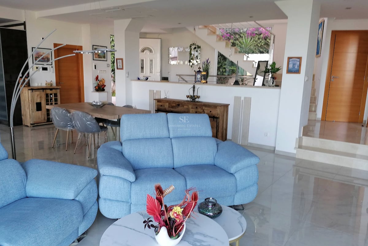 Un grand salon avec des canapés bleus, un sol en marbre poli et un coin repas adjacent dans une villa moderne.