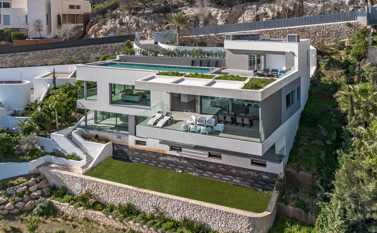 Vue aérienne d'une villa moderne blanche à plusieurs niveaux avec une piscine à débordement sur le toit.