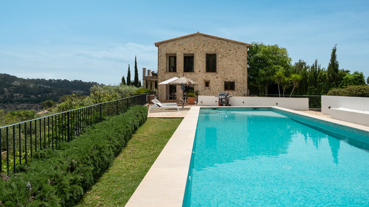 Piscine turquoise et façade en pierre naturelle d'une villa méditerranéenne avec jardin et transats.