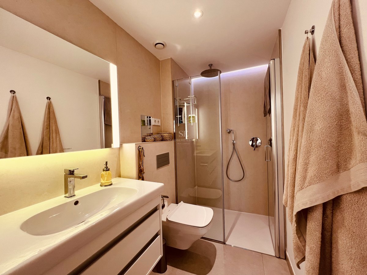 Salle de bain contemporaine avec douche vitrée, meuble vasque suspendu et éclairage LED chaleureux.