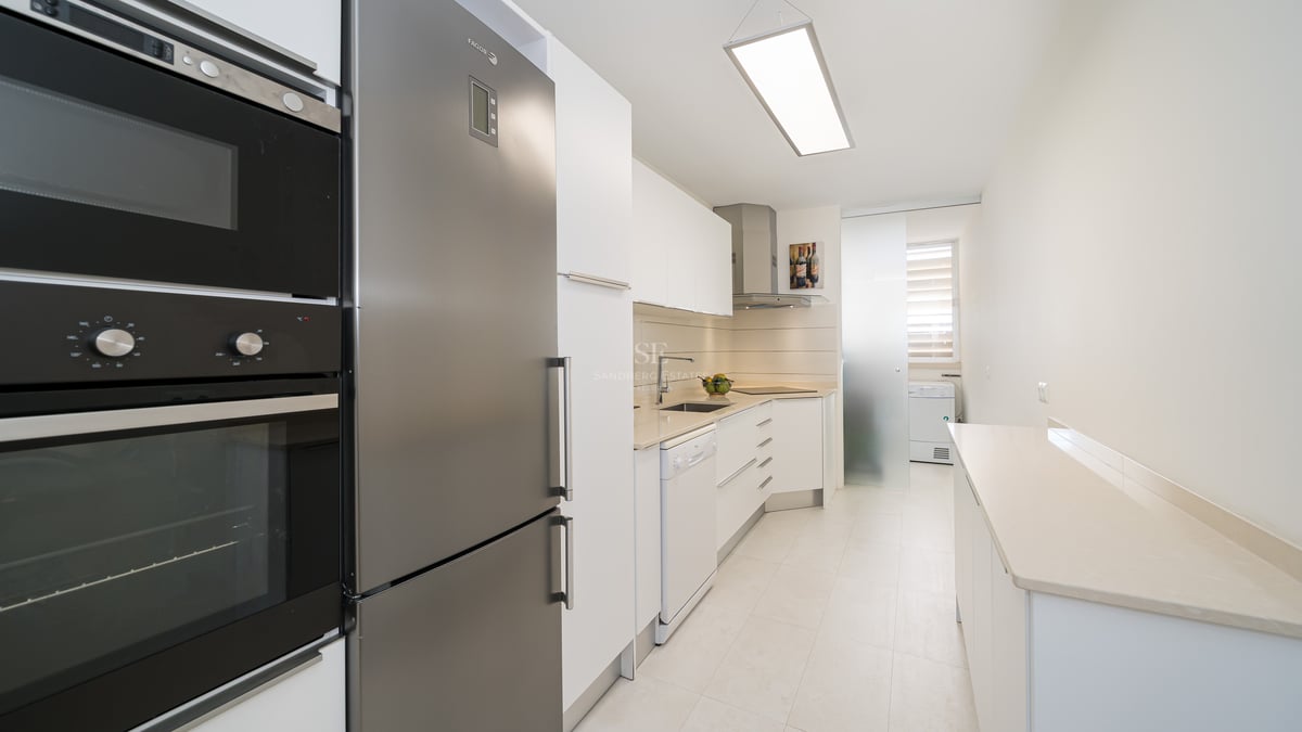 A modern galley-style kitchen with white cabinetry and stainless steel appliances.