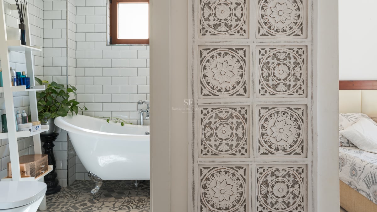 Salle de bain avec baignoire à pattes blanche, carrelage métro et sol à motifs, vue à travers une porte en bois sculpté.