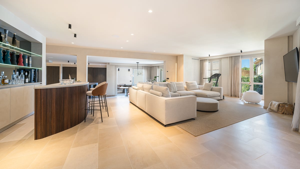 Salon moderne avec un grand canapé d'angle crème, sol en pierre naturelle et bar en bois courbé.