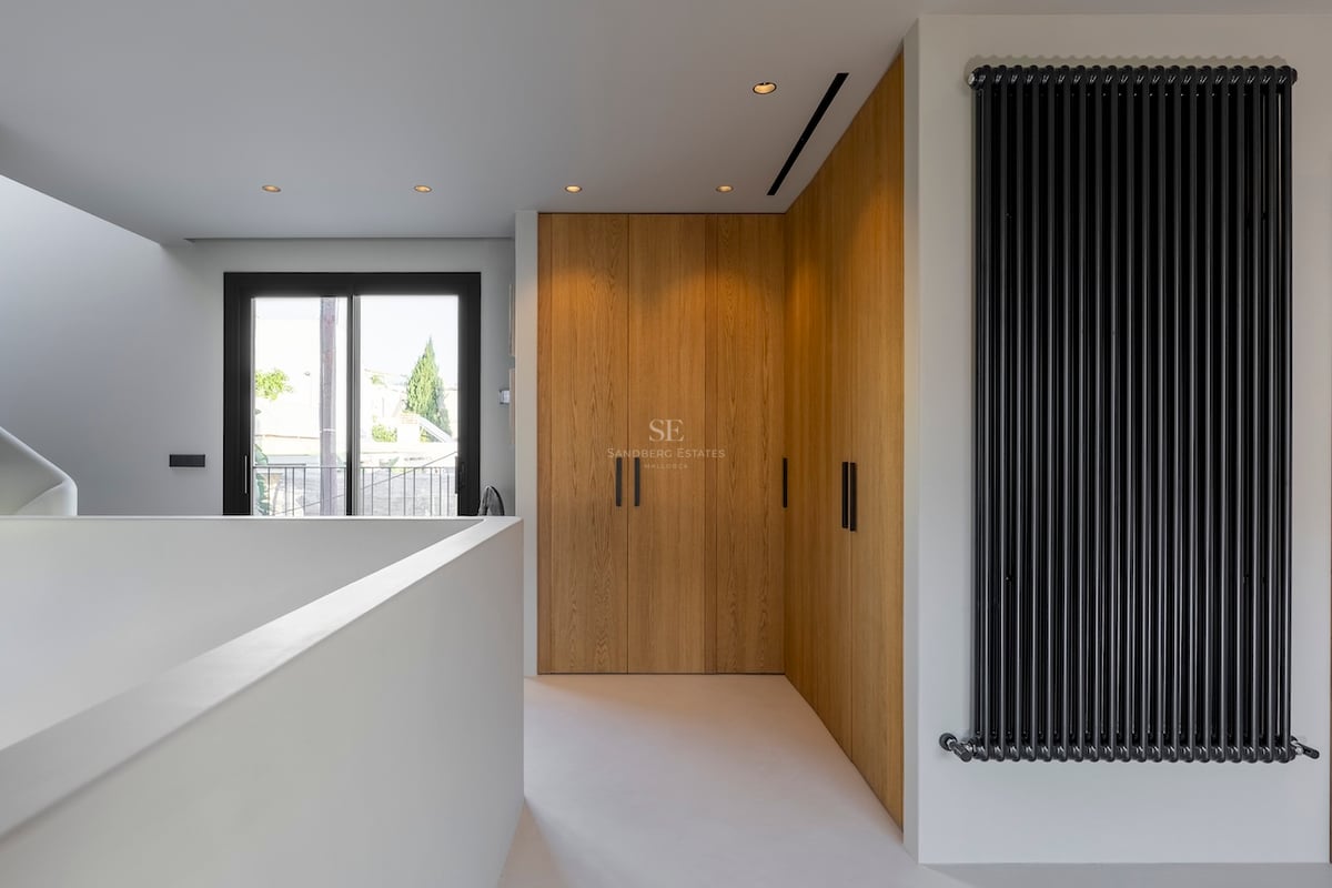 Couloir avec armoires en bois du sol au plafond, radiateur noir vertical et porte vitrée menant au balcon.