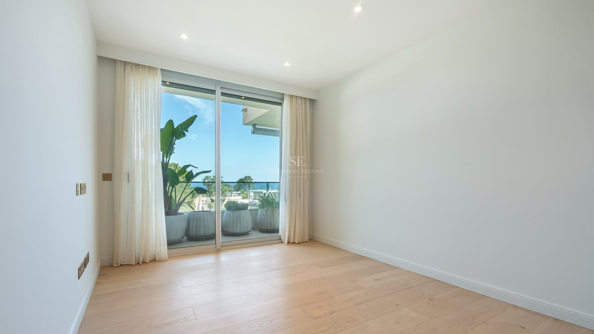 Empty modern room featuring light wood floors and large sliding glass doors opening to a terrace with sea views.