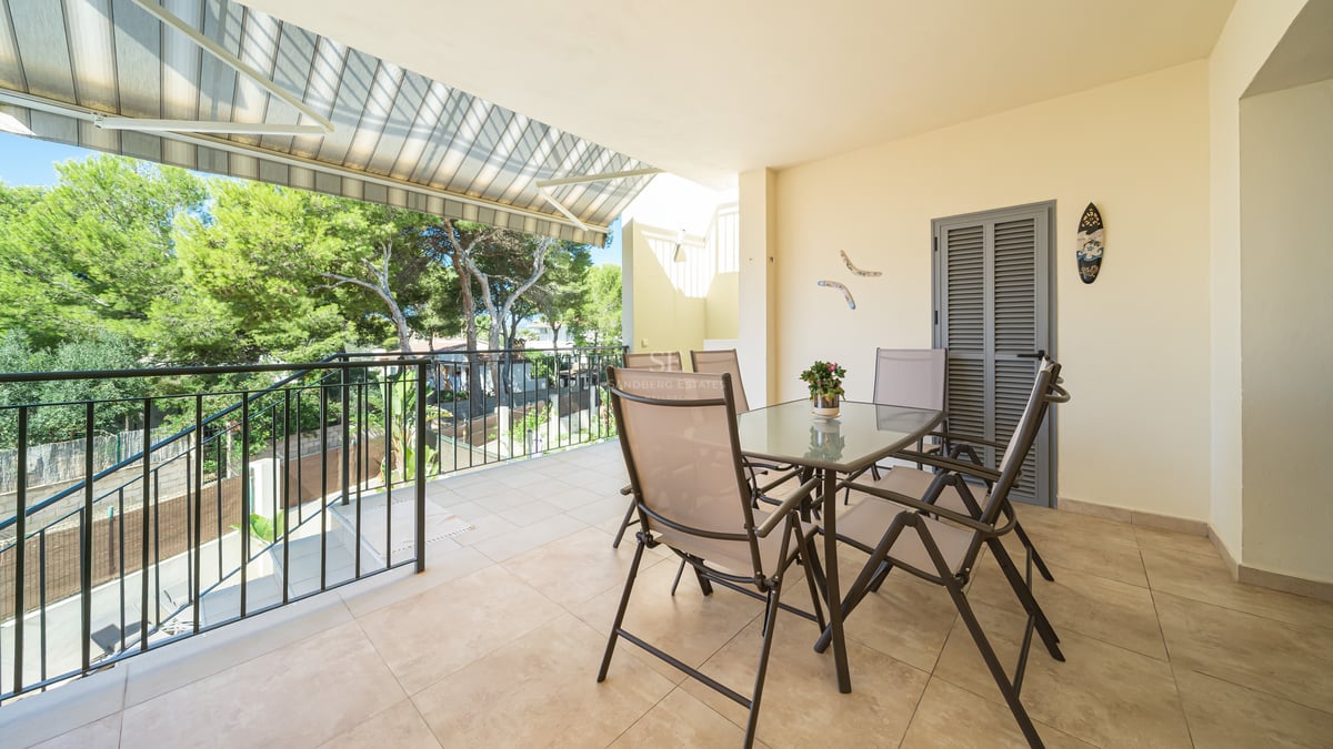 Kaklad balkong med matbord och stolar under en markis med utsikt över lummiga tallar.