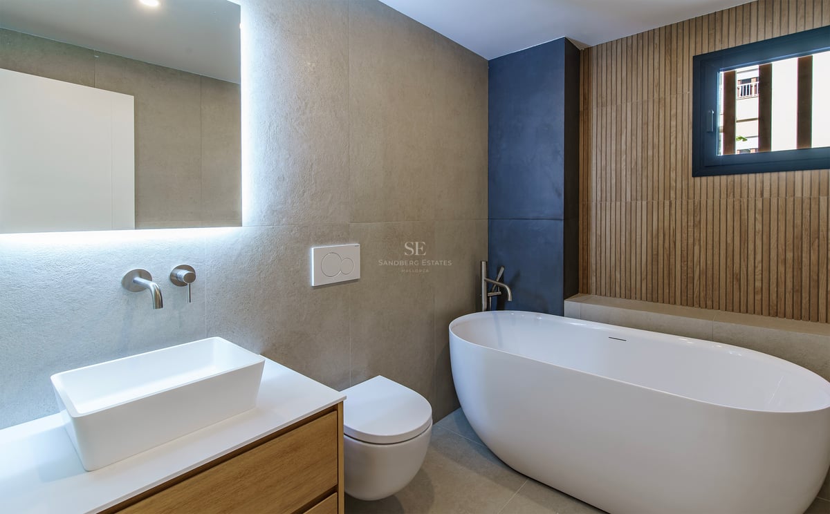 Salle de bain moderne avec baignoire îlot, vasque sur meuble en bois et miroir rétroéclairé.