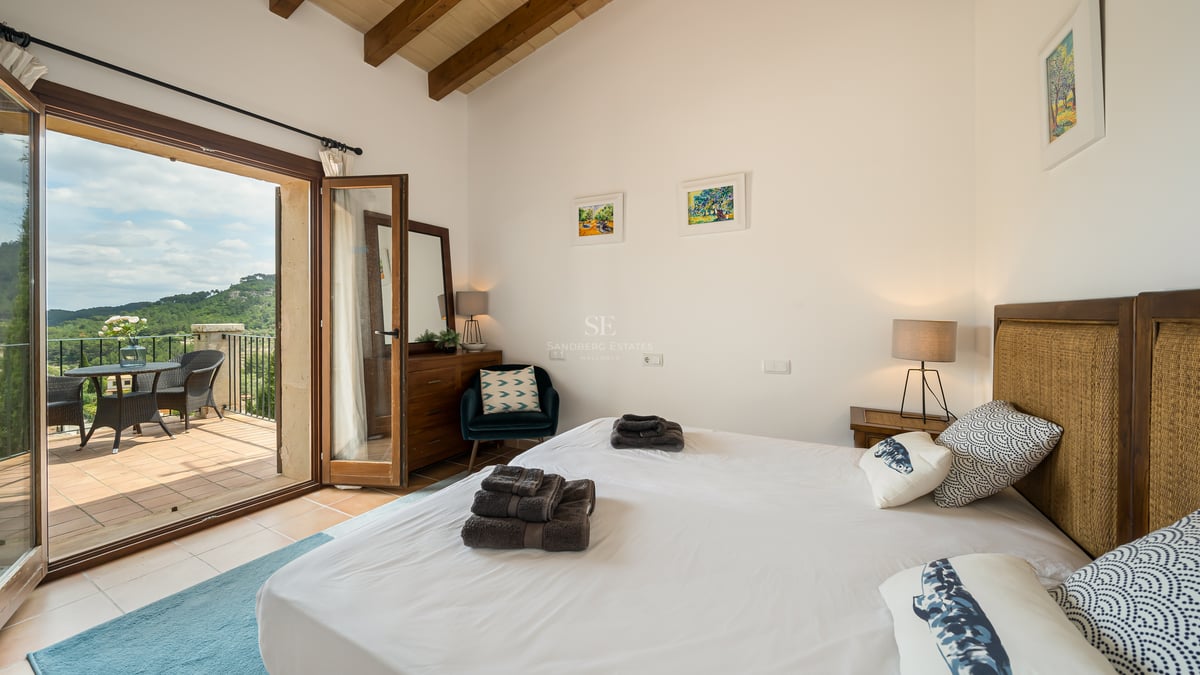 Chambre lumineuse avec poutres en bois, literie blanche et porte vitrée donnant sur une terrasse.