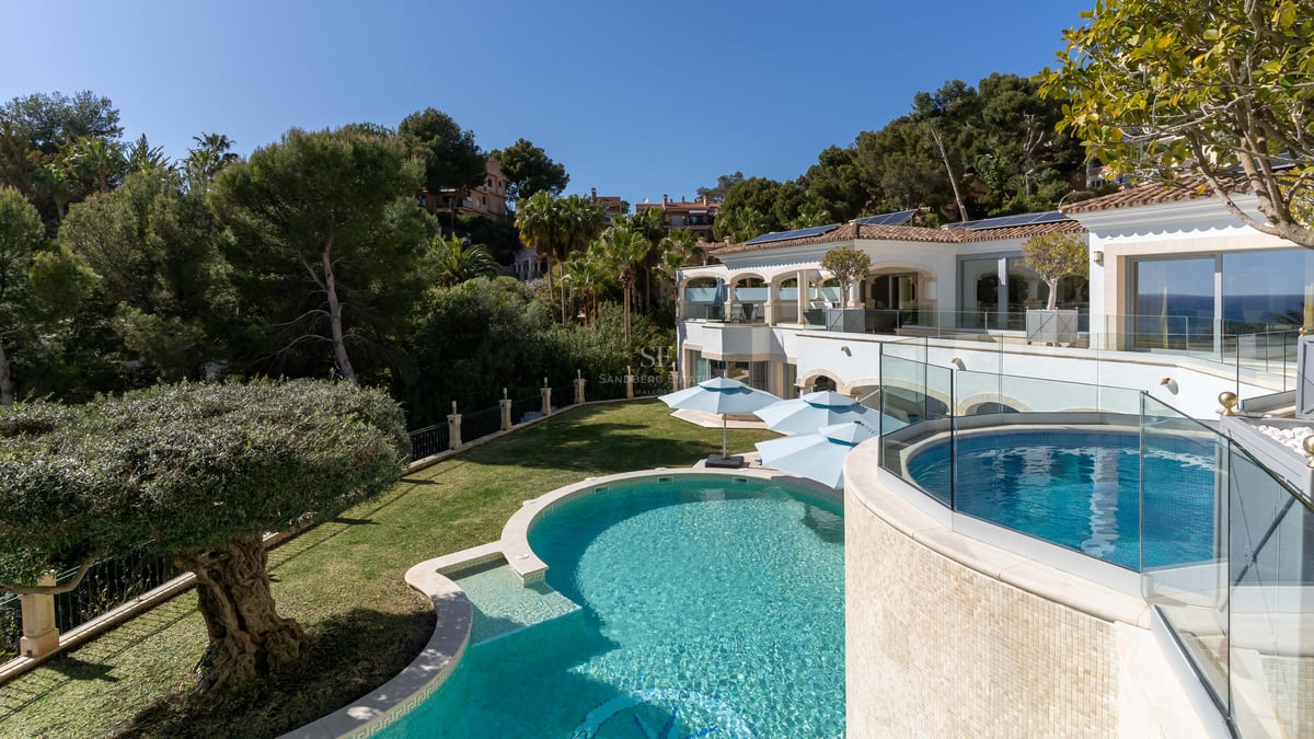 Luxusvilla mit geschwungenem türkisblauem Pool, Glasgeländern und üppigem Grün auf Mallorca.