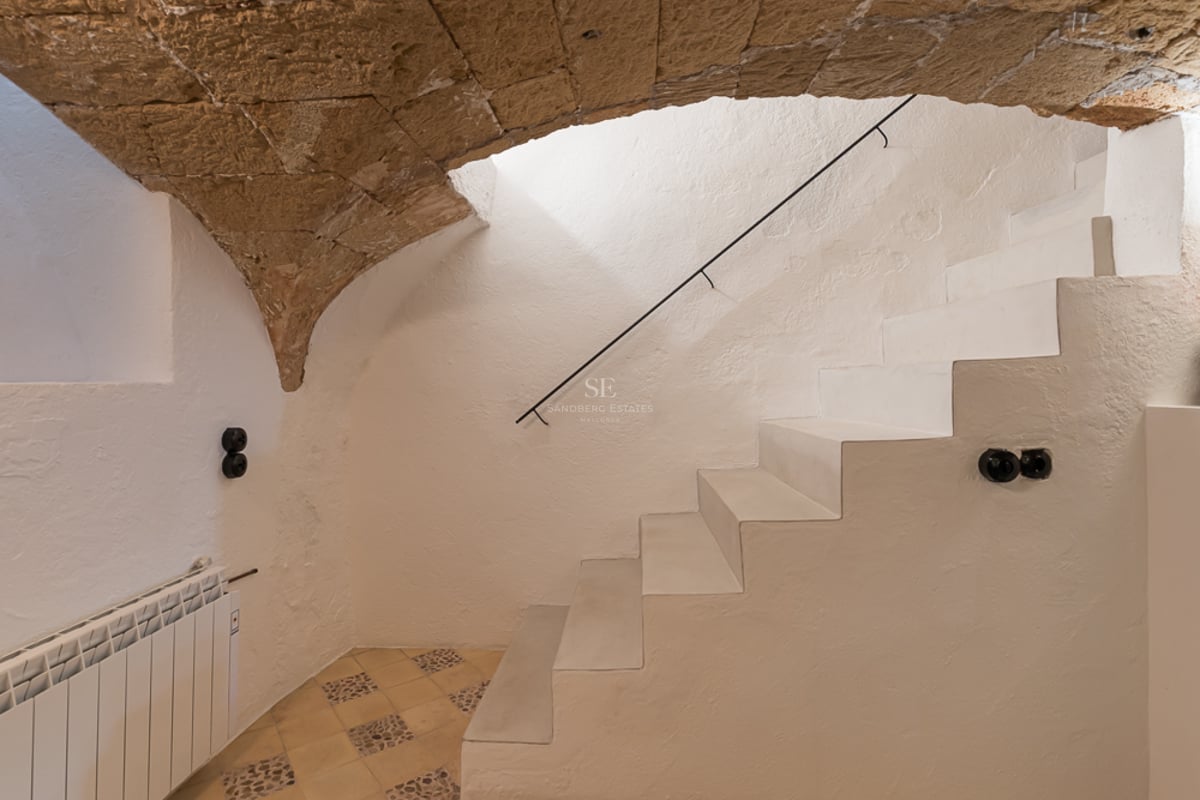 Escalier blanc minimaliste sous une voûte en pierre naturelle dans une maison rénovée à Majorque.