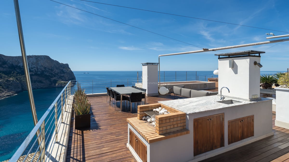 Luxury rooftop terrace featuring an outdoor kitchen, dining area, and panoramic views of a Mediterranean bay.