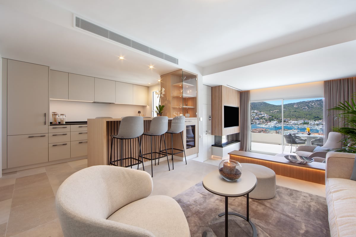 Salon et cuisine ouverts et modernes avec des armoires beiges et une grande fenêtre donnant sur un port de plaisance.