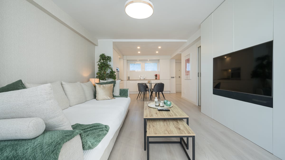 Bright modern living room featuring a white sofa, light wood floors, and a large flat-screen TV integrated into white cabinetry.