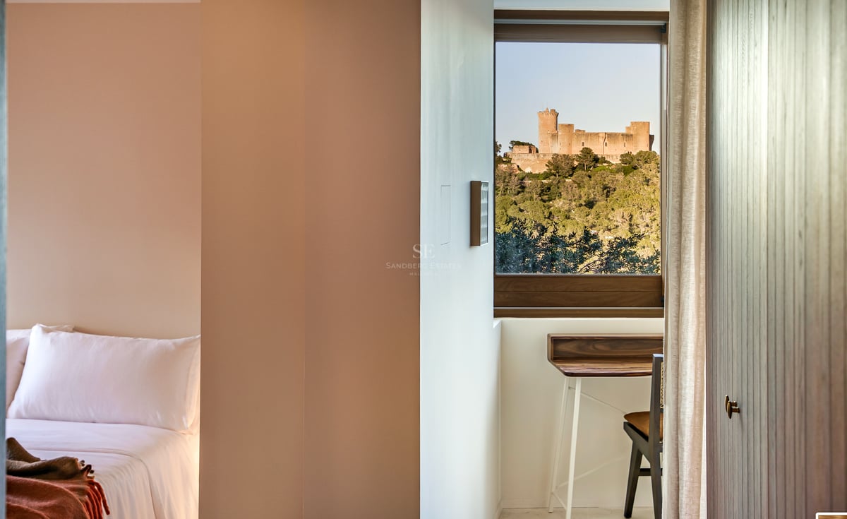 Modernes Schlafzimmerfenster mit Blick auf eine mittelalterliche Burg auf einem bewaldeten Hügel und einem Schreibtisch.