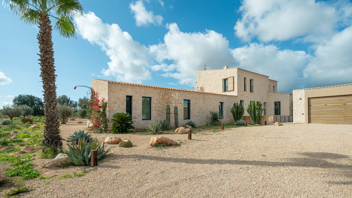 Naturstensfasad på en modern villa med kaktusträdgård och grusuppfart under en klarblå himmel.